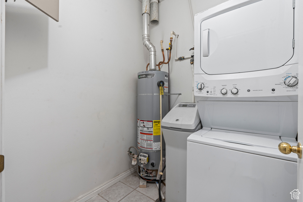 Laundry room with water heater, light tile floors, and stacked washing maching and dryer