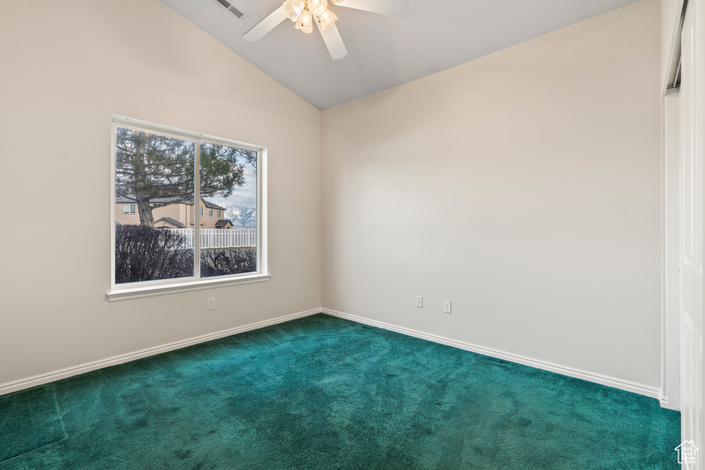Empty room with lofted ceiling, dark colored carpet, and ceiling fan