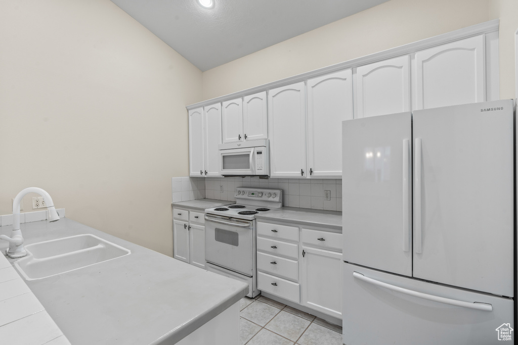 Kitchen with sink, white appliances, backsplash, and white cabinets