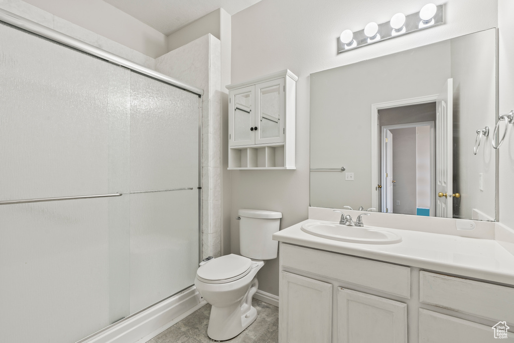 Bathroom featuring toilet, tile flooring, a shower with shower door, and vanity with extensive cabinet space