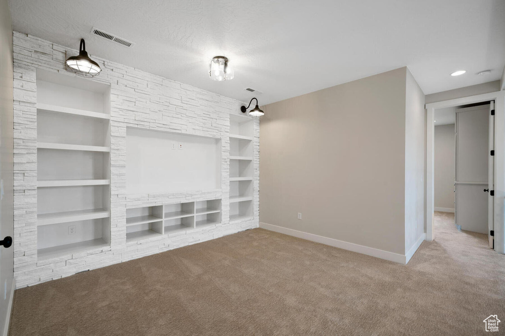 Unfurnished room featuring a textured ceiling, built in shelves, and light colored carpet