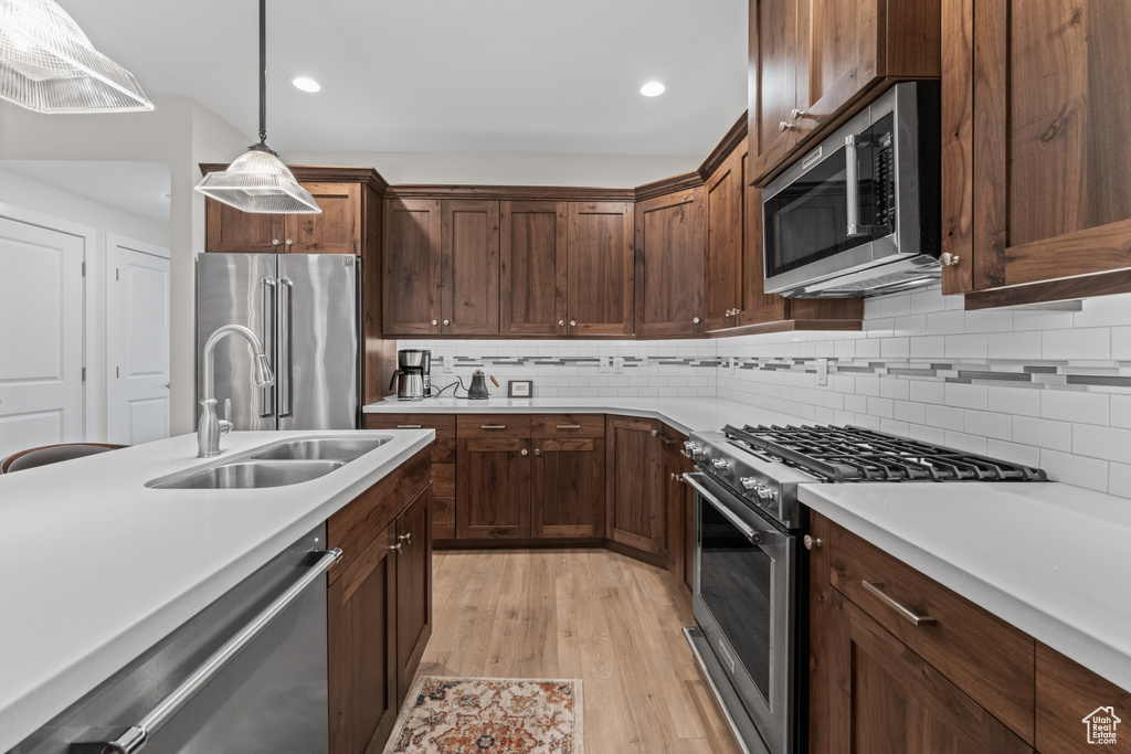 Kitchen with sink, premium appliances, light hardwood / wood-style floors, hanging light fixtures, and backsplash