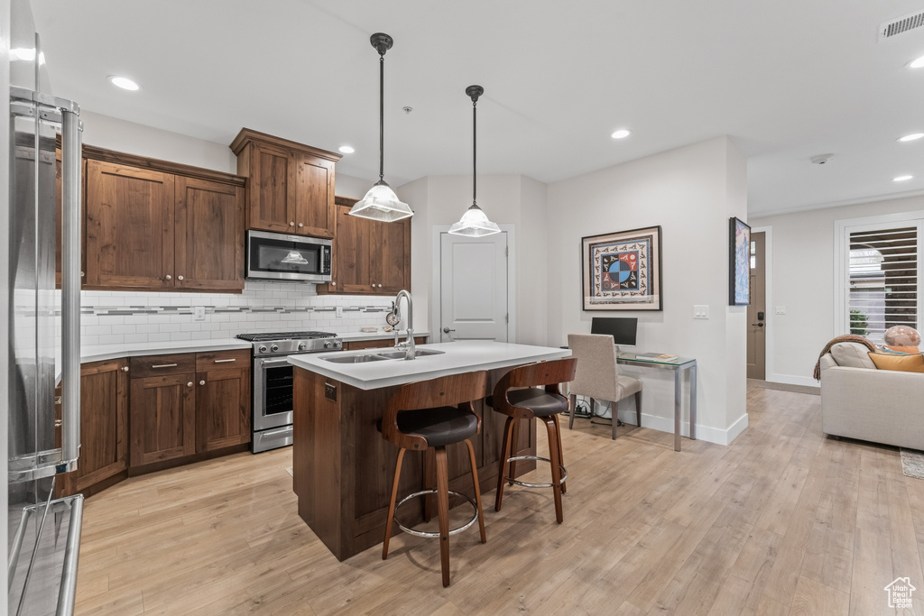 Kitchen featuring sink, high end appliances, backsplash, light hardwood / wood-style floors, and hanging light fixtures