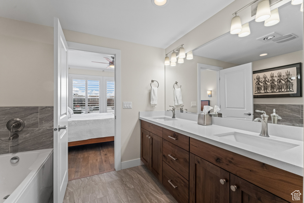 Bathroom featuring hardwood / wood-style flooring, tiled tub, double vanity, and ceiling fan