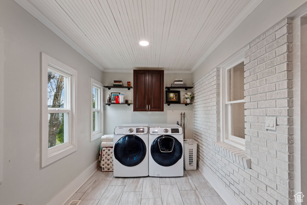 Laundry area featuring cabinets, washing machine and dryer, a wealth of natural light, crown molding, and brick wall