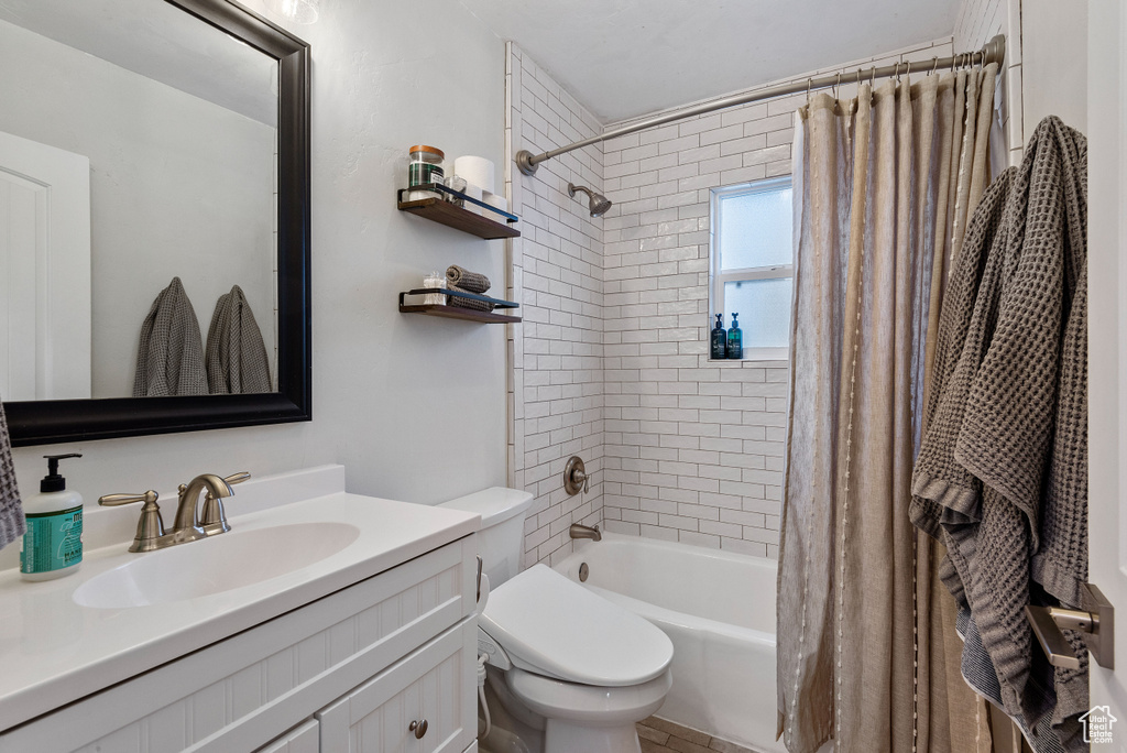 Full bathroom with shower / bathtub combination with curtain, oversized vanity, and toilet