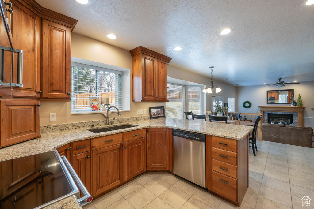 Kitchen featuring stove, dishwasher, sink, ceiling fan with notable chandelier, and light stone countertops