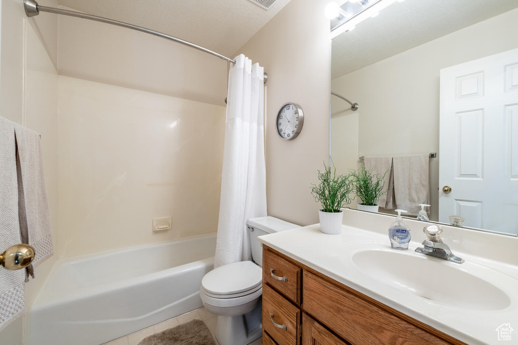 Full bathroom with a textured ceiling, shower / tub combo, toilet, tile floors, and large vanity