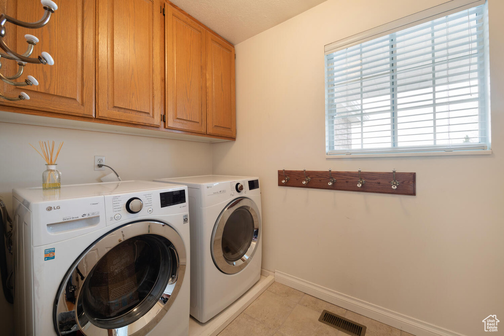 Washroom with light tile flooring, a wealth of natural light, cabinets, and independent washer and dryer