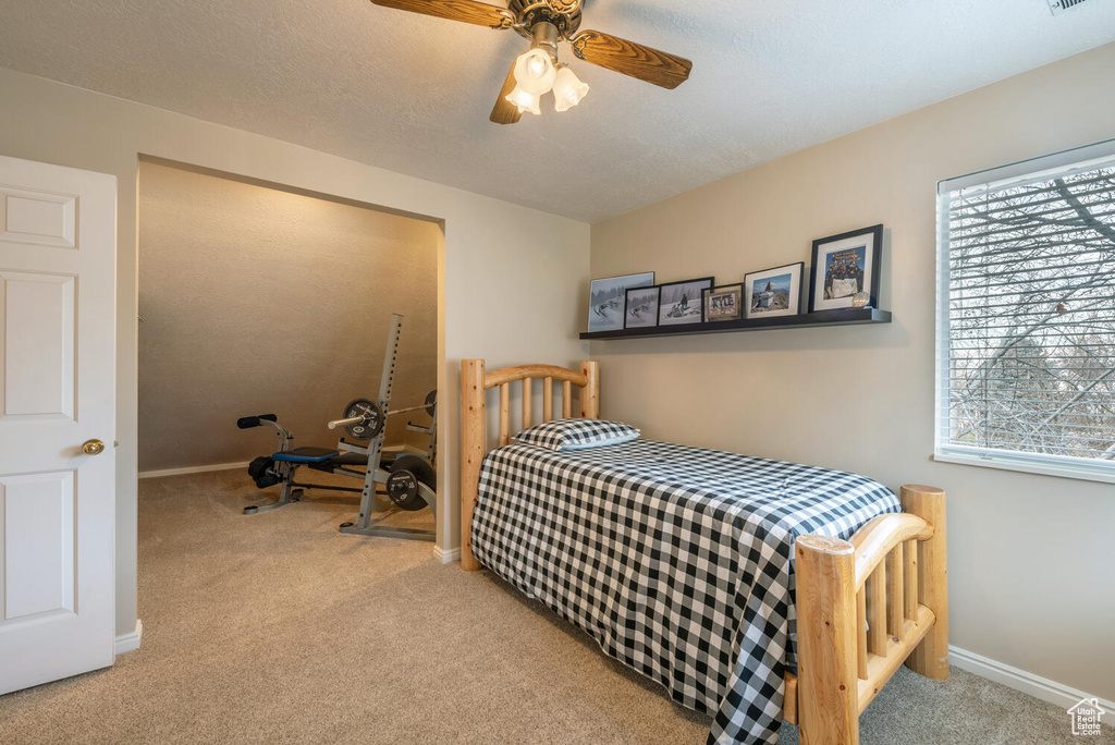 Bedroom with light colored carpet, a textured ceiling, multiple windows, and ceiling fan