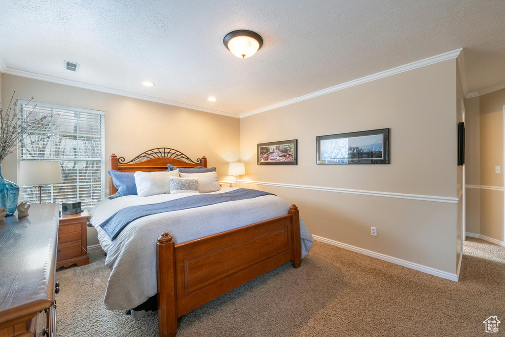 Bedroom featuring a textured ceiling, ornamental molding, and light colored carpet
