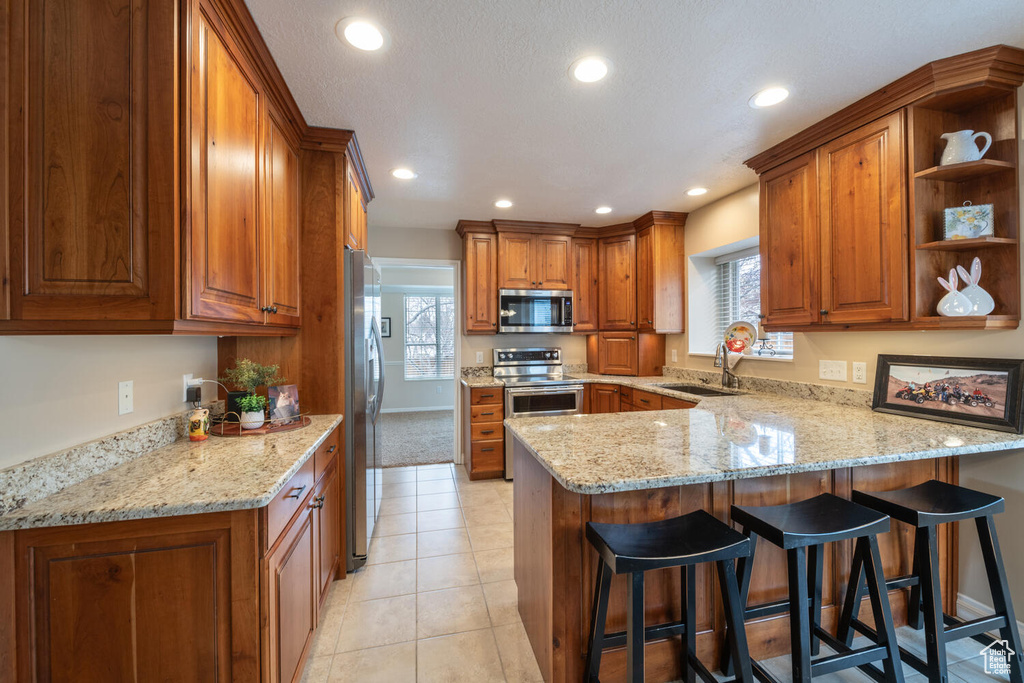 Kitchen featuring sink, a kitchen breakfast bar, light tile floors, appliances with stainless steel finishes, and light stone counters