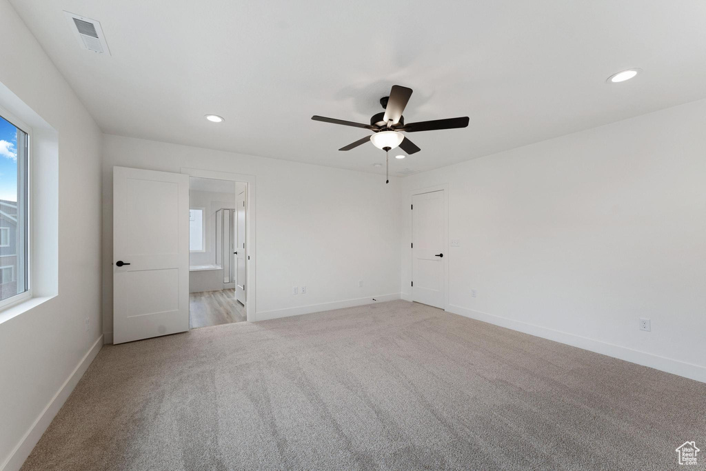 Empty room featuring a wealth of natural light, light colored carpet, and ceiling fan