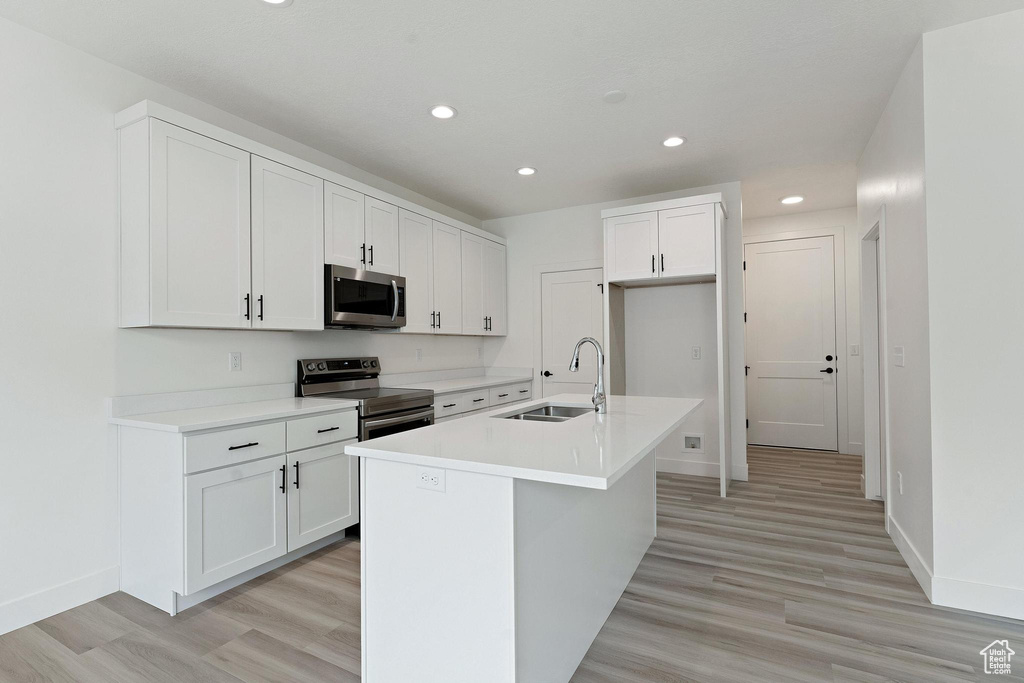 Kitchen with white cabinetry, appliances with stainless steel finishes, sink, and a center island with sink