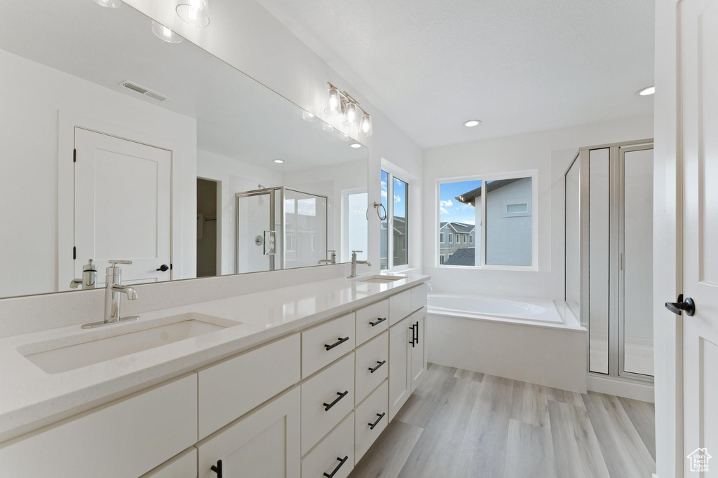 Bathroom featuring dual vanity, shower with separate bathtub, and hardwood / wood-style floors