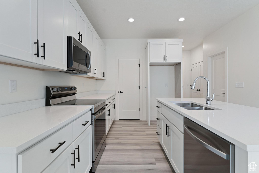 Kitchen featuring appliances with stainless steel finishes, light wood-type flooring, white cabinets, and sink