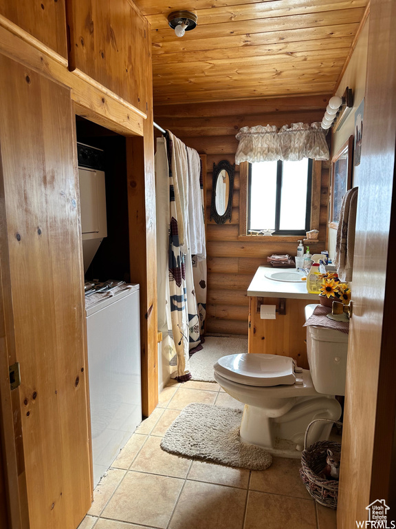 Bathroom featuring stacked washer and dryer, rustic walls, tile floors, vanity, and toilet