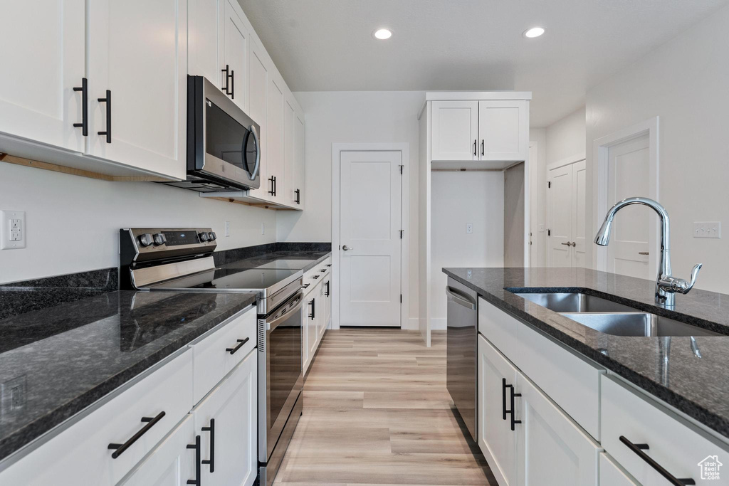 Kitchen featuring sink, appliances with stainless steel finishes, light hardwood / wood-style floors, white cabinets, and dark stone counters