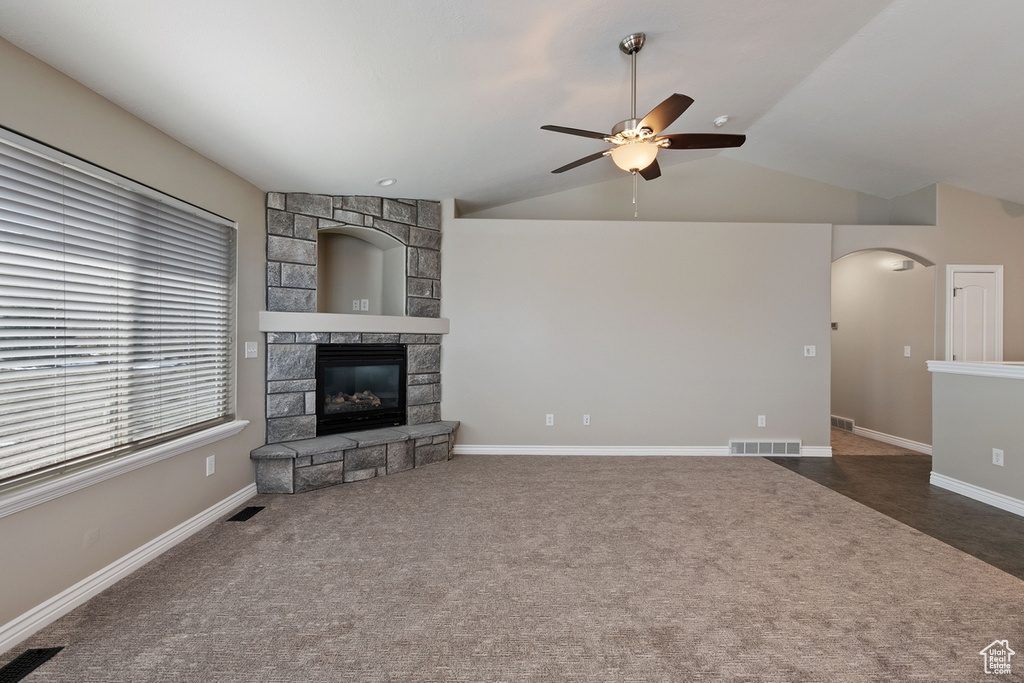 Carpeted living room featuring lofted ceiling, a stone fireplace, and ceiling fan