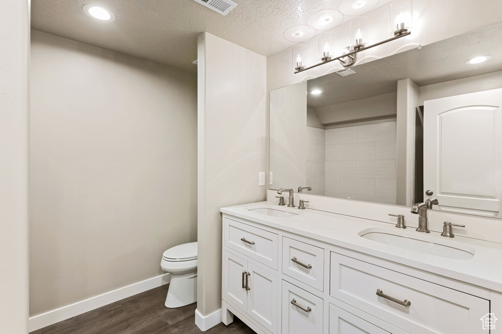 Bathroom featuring hardwood / wood-style floors, toilet, a textured ceiling, and dual vanity
