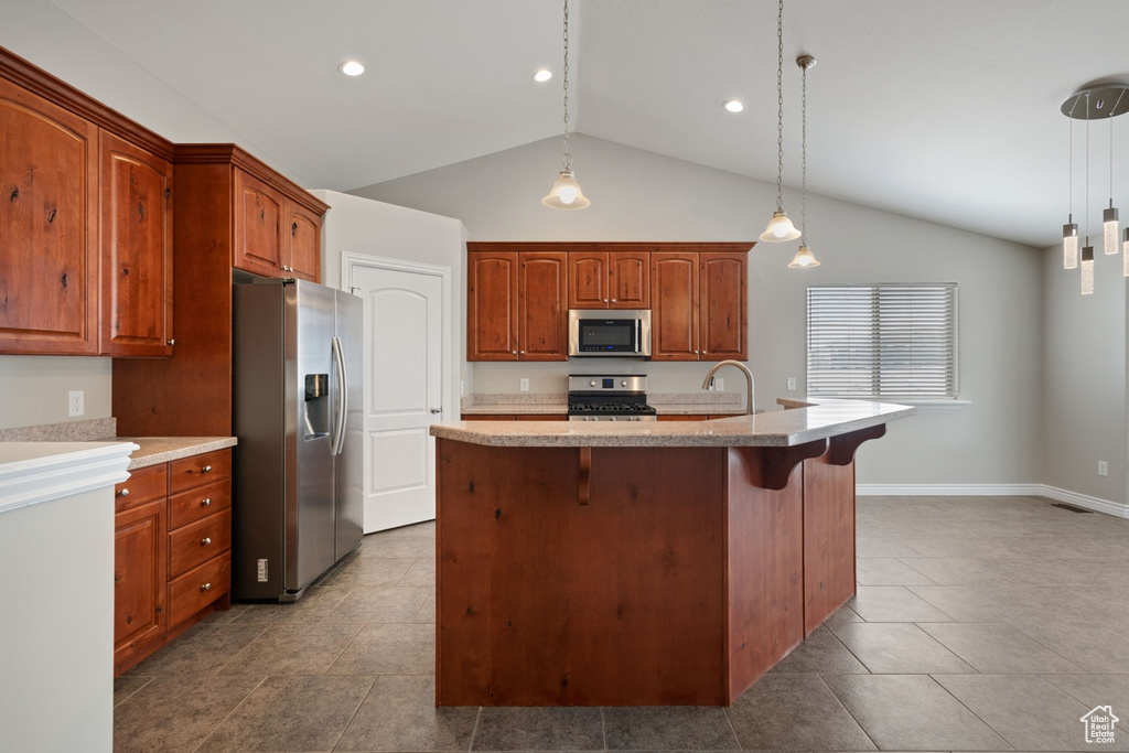 Kitchen with vaulted ceiling, decorative light fixtures, dark tile floors, and appliances with stainless steel finishes