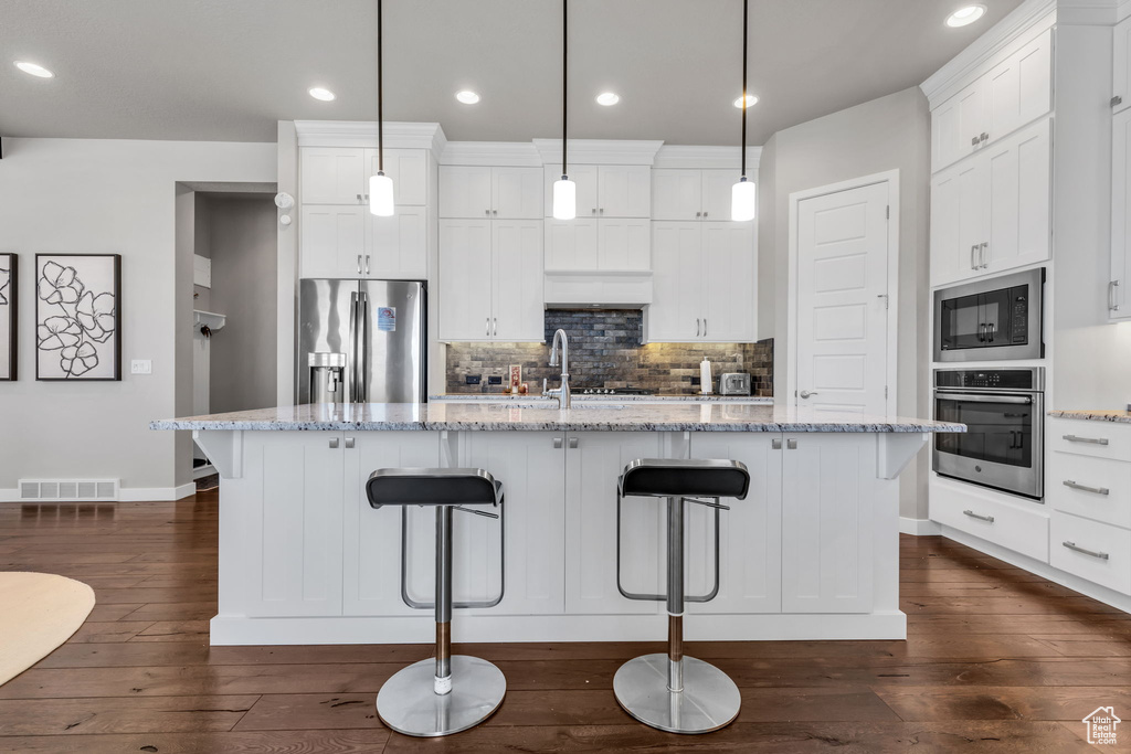 Kitchen with appliances with stainless steel finishes, white cabinetry, dark hardwood / wood-style floors, and hanging light fixtures