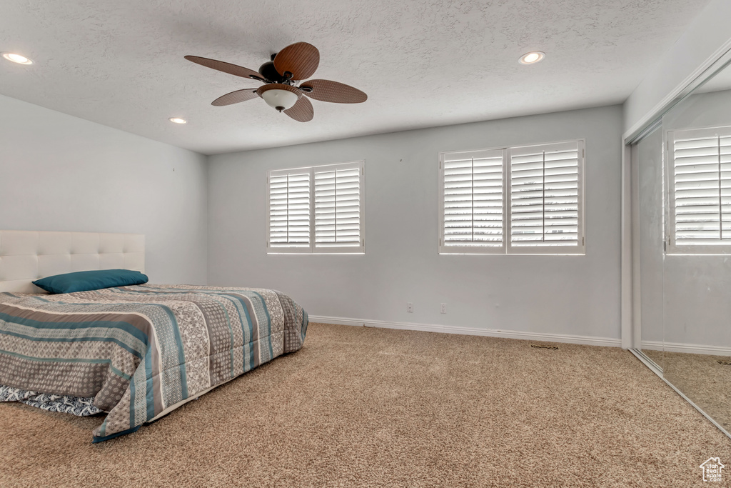 Bedroom featuring light colored carpet, a textured ceiling, ceiling fan, and a closet