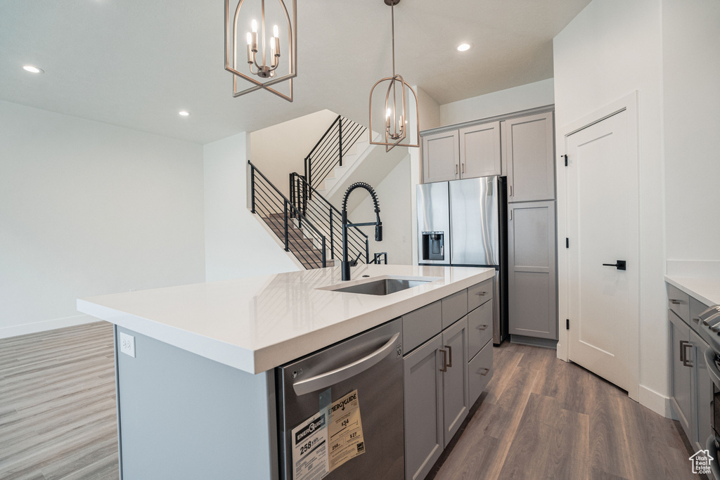 Kitchen featuring gray cabinetry, appliances with stainless steel finishes, a chandelier, a kitchen island with sink, and dark hardwood / wood-style floors