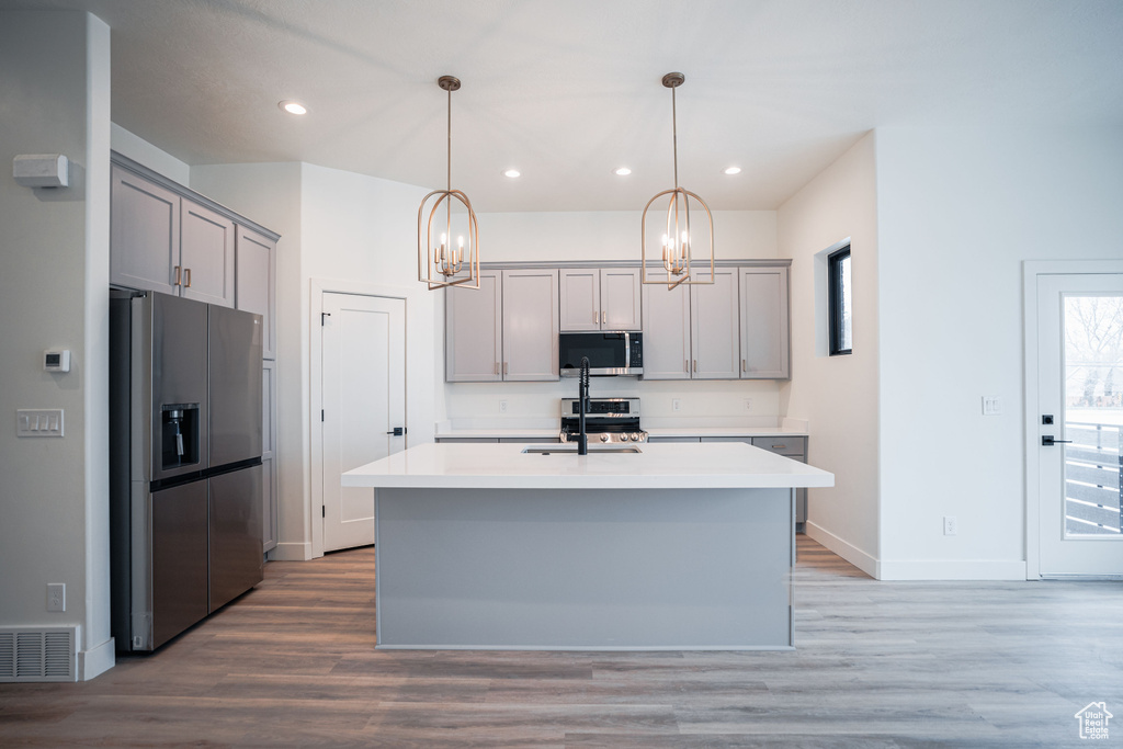 Kitchen featuring appliances with stainless steel finishes, gray cabinets, hanging light fixtures, and light hardwood / wood-style flooring