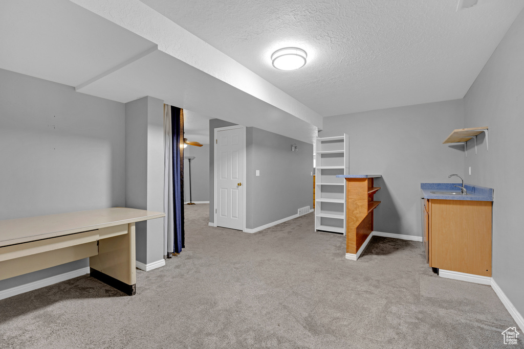 Unfurnished bedroom with a textured ceiling, light colored carpet, and sink