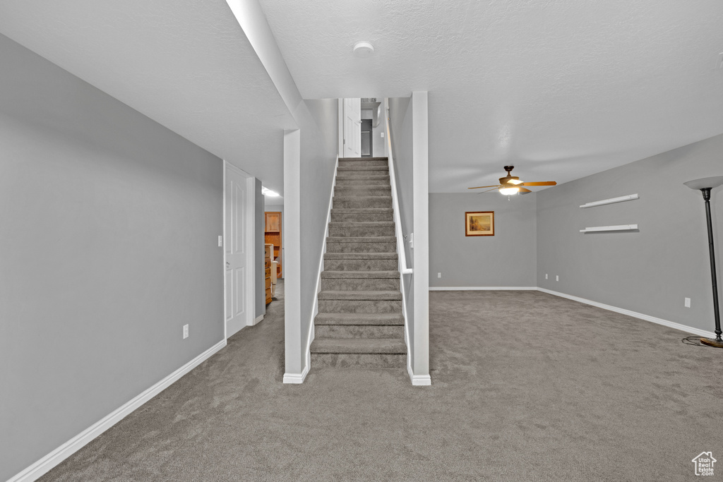 Staircase featuring dark carpet and ceiling fan