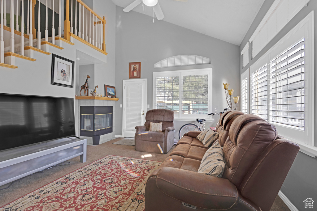 Living room featuring a tile fireplace, high vaulted ceiling, carpet floors, and ceiling fan