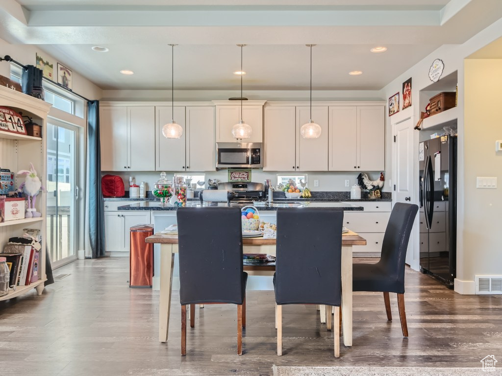 Kitchen featuring hardwood / wood-style flooring, pendant lighting, black fridge with ice dispenser, and a breakfast bar area