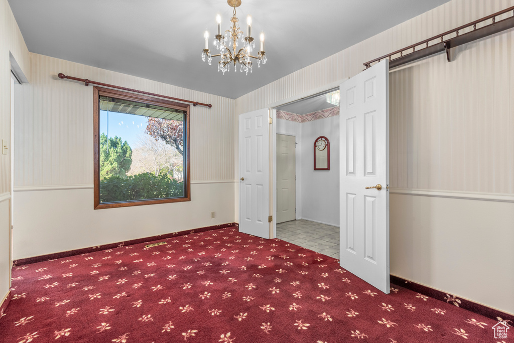 Unfurnished room featuring dark colored carpet and an inviting chandelier