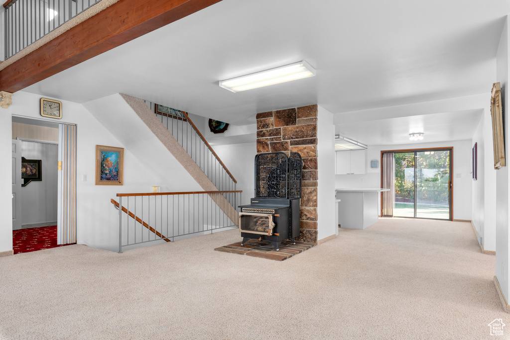 Unfurnished living room featuring a wood stove, light carpet, and beamed ceiling