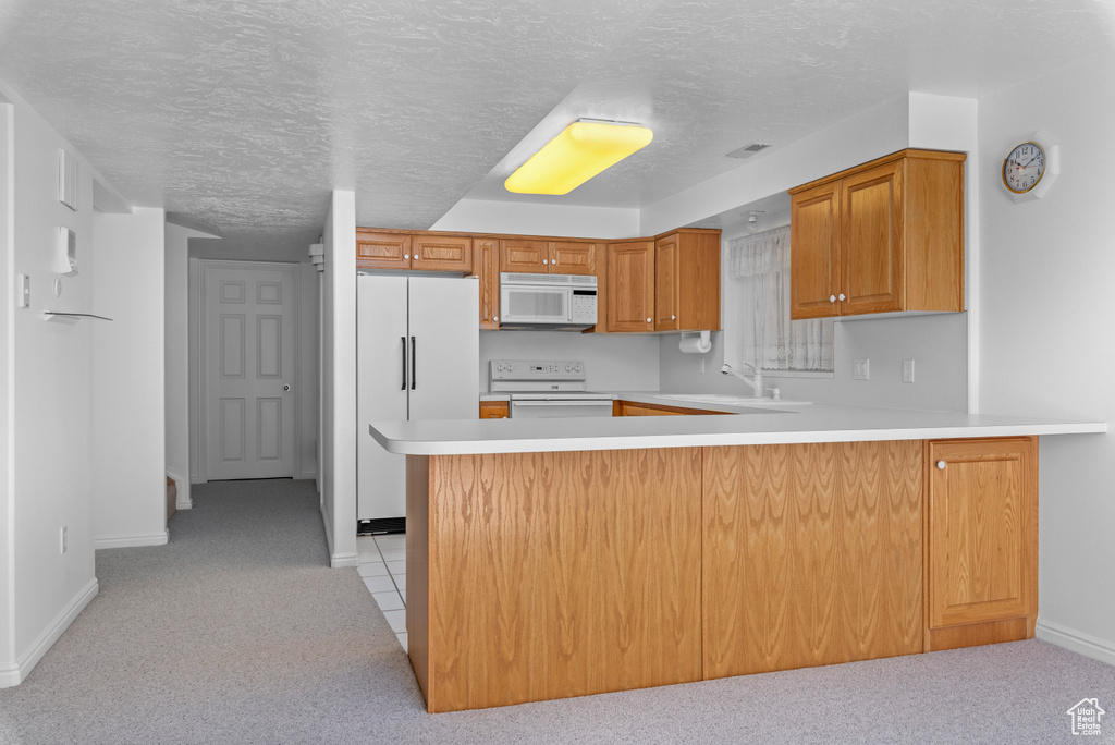 Kitchen featuring a textured ceiling, light carpet, kitchen peninsula, white appliances, and sink