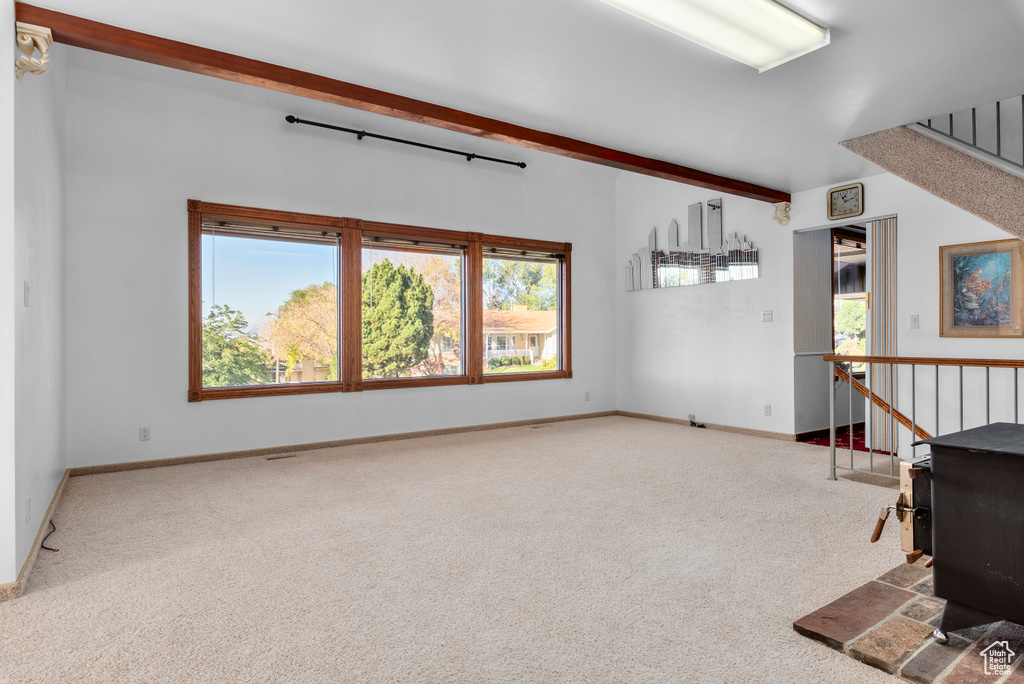 Unfurnished living room featuring light colored carpet, a wood stove, and beamed ceiling