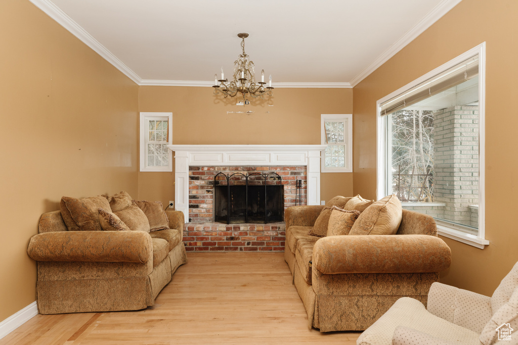 Living room featuring an inviting chandelier, a brick fireplace, light hardwood / wood-style floors, and crown molding