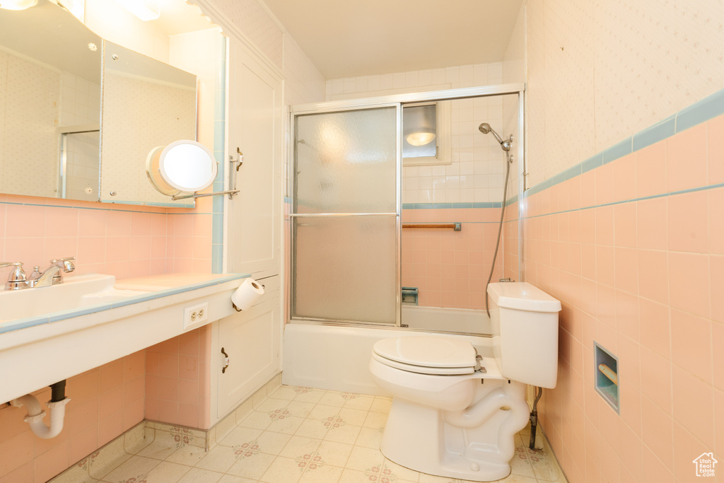 Bathroom featuring bath / shower combo with glass door, tile walls, backsplash, toilet, and tile flooring
