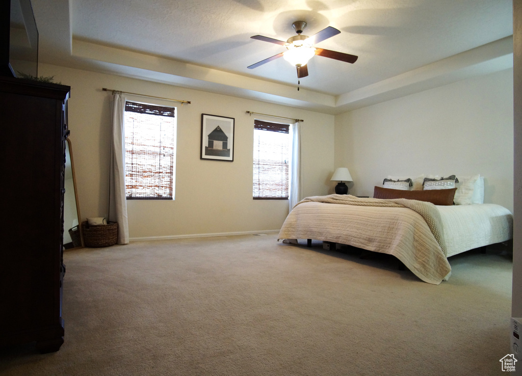 Bedroom featuring dark colored carpet, multiple windows, a tray ceiling, and ceiling fan