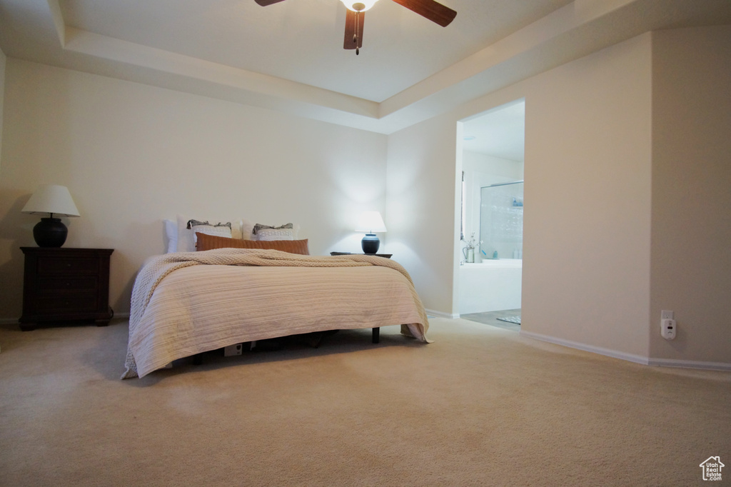 Carpeted bedroom with connected bathroom, ceiling fan, and a tray ceiling