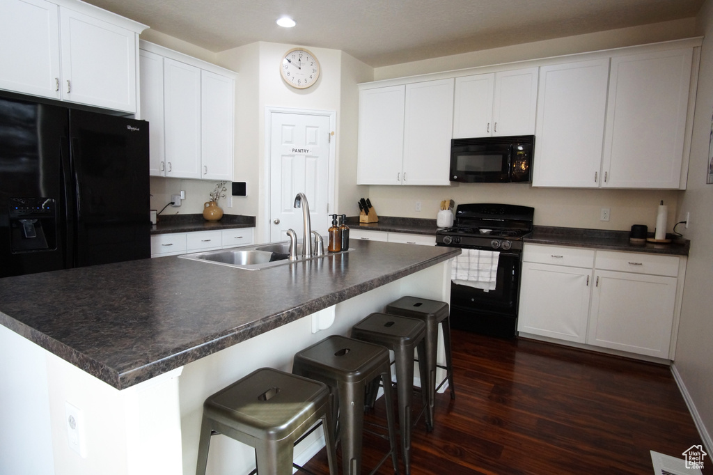 Kitchen with white cabinets, a kitchen breakfast bar, a kitchen island with sink, dark wood-type flooring, and black appliances