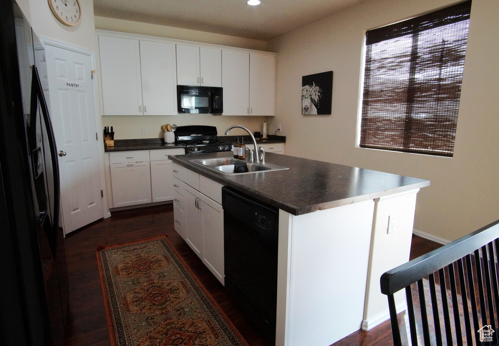 Kitchen featuring black appliances, dark hardwood / wood-style flooring, white cabinetry, and a center island with sink