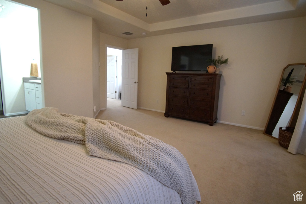 Carpeted bedroom with a tray ceiling, ensuite bath, and ceiling fan