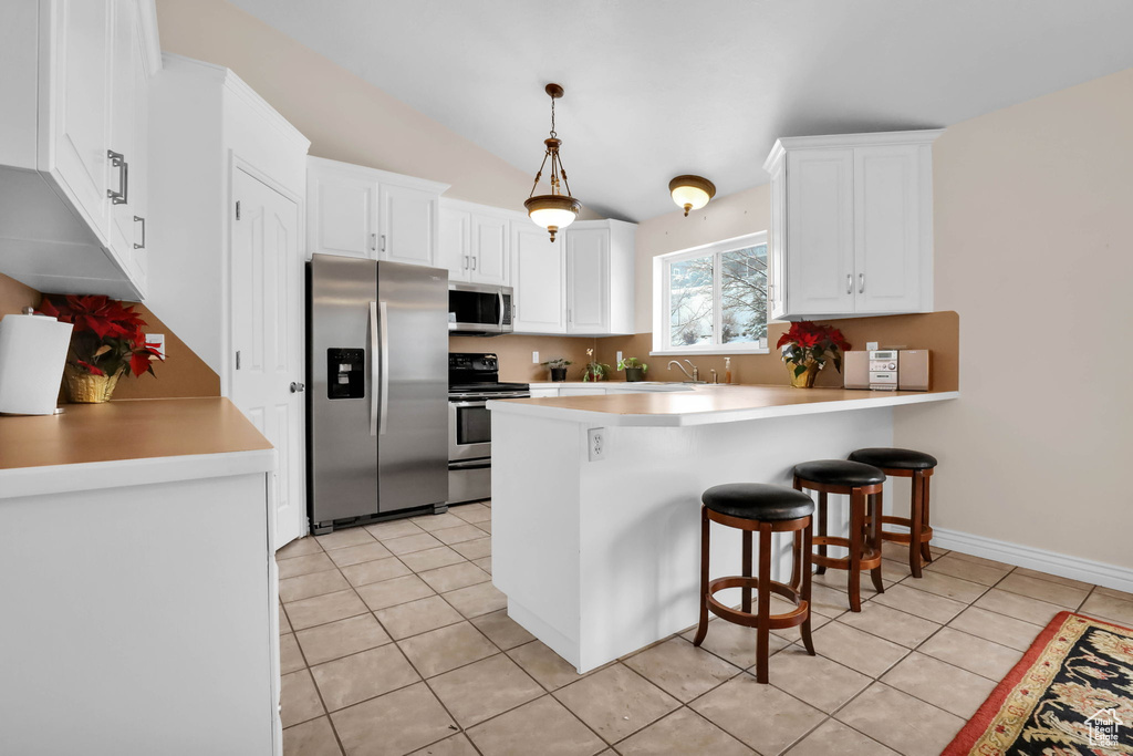 Kitchen with white cabinets, light tile floors, stainless steel appliances, and decorative light fixtures