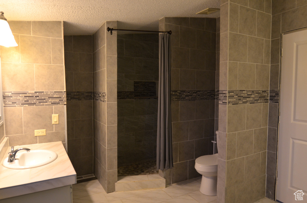 Bathroom with a tile shower, tile floors, tile walls, and vanity