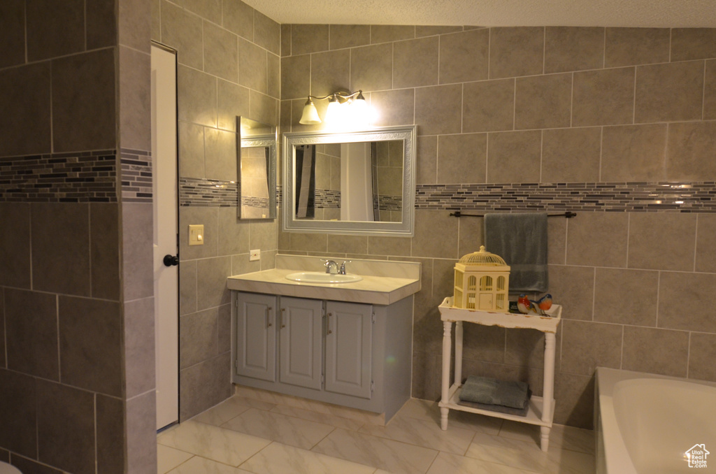 Bathroom featuring a textured ceiling, tile walls, vanity, a bathtub, and tile flooring