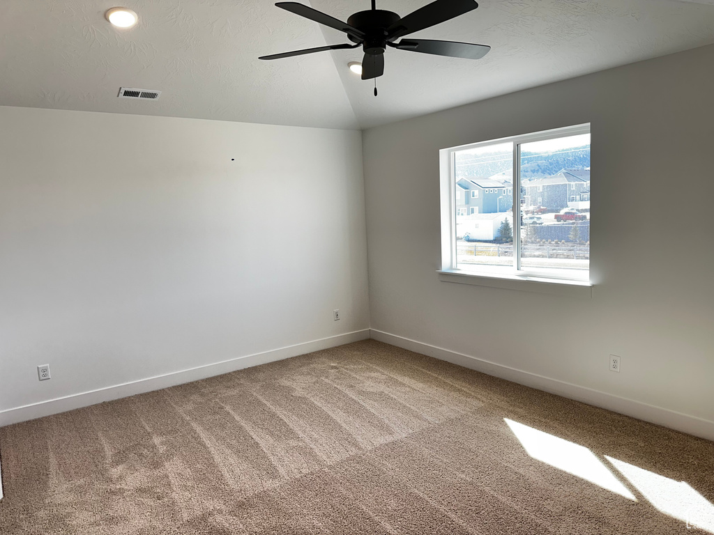 Spare room featuring vaulted ceiling, light colored carpet, and ceiling fan