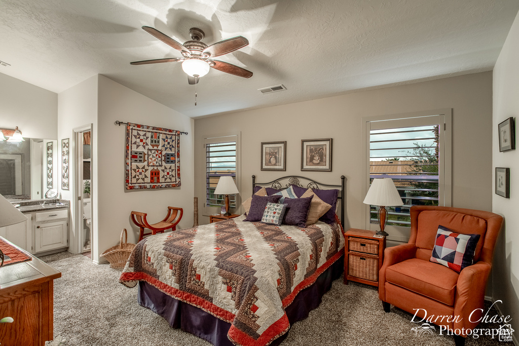 Carpeted bedroom featuring multiple windows, ensuite bath, a textured ceiling, and ceiling fan