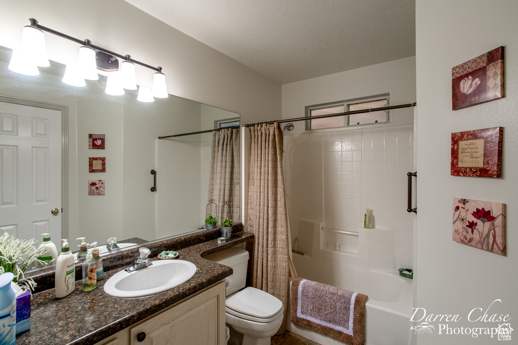 Full bathroom featuring shower / bath combination with curtain, vanity, toilet, and a textured ceiling